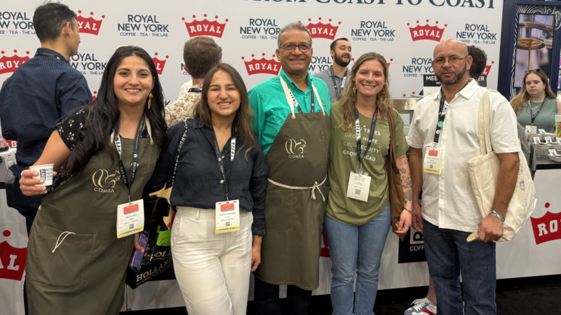 3 women and 2 men standing in front of an expo booth smiling.