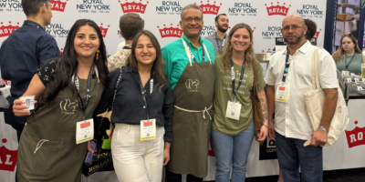 3 women and 2 men standing in front of an expo booth smiling.